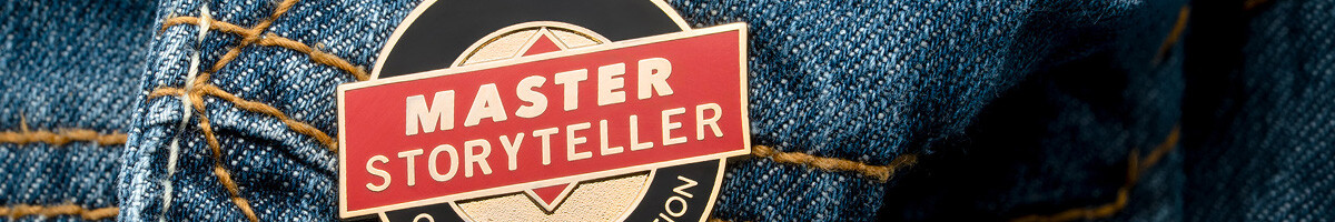 Red and black Master Storyteller Official Designation hard enamel pin on a denim jacket