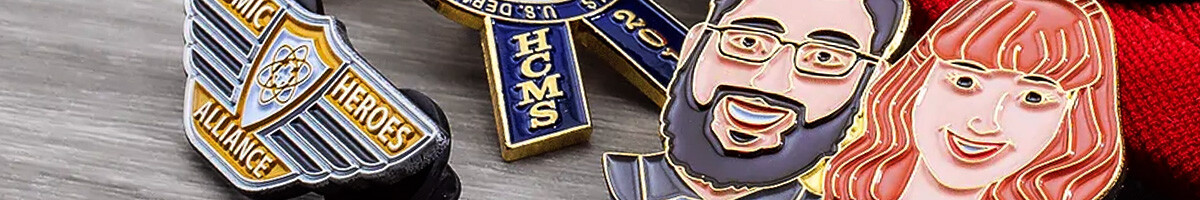 A collection of custom enamel pins including an Atomic Alliance Heroes shield, HCMS ribbon pins, and two portrait pins of a bearded man and a woman with long hair