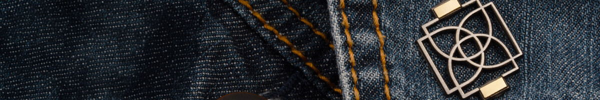 Dual plated die struck pin with a silver geometric knot design and gold accents on a denim jacket