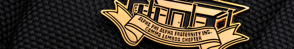 Gold Alpha Phi Alpha Fraternity Gamma Lambda Chapter pin shaped like the chapter house on black fabric