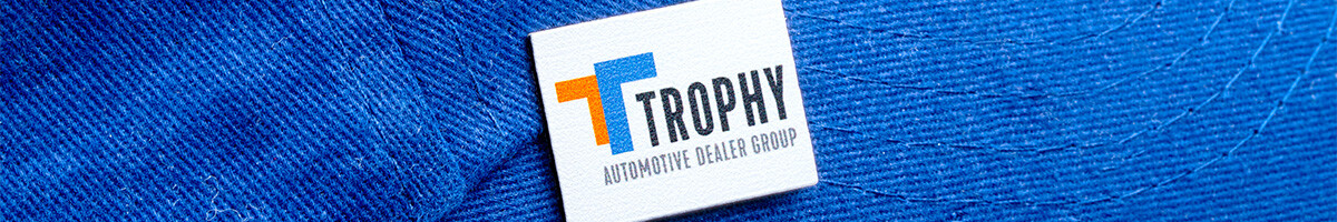 A white square Trophy Automotive Dealer Group printed rush pin on a royal blue cap