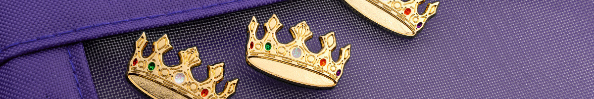 Three gold crown lapel pins set with red, green, and white rhinestones on purple nylon