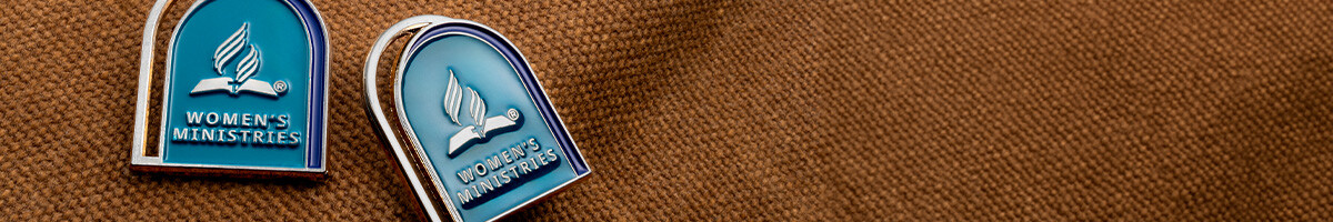 Teal and navy arch-shaped Women's Ministries lapel pins with a silver outline on brown canvas